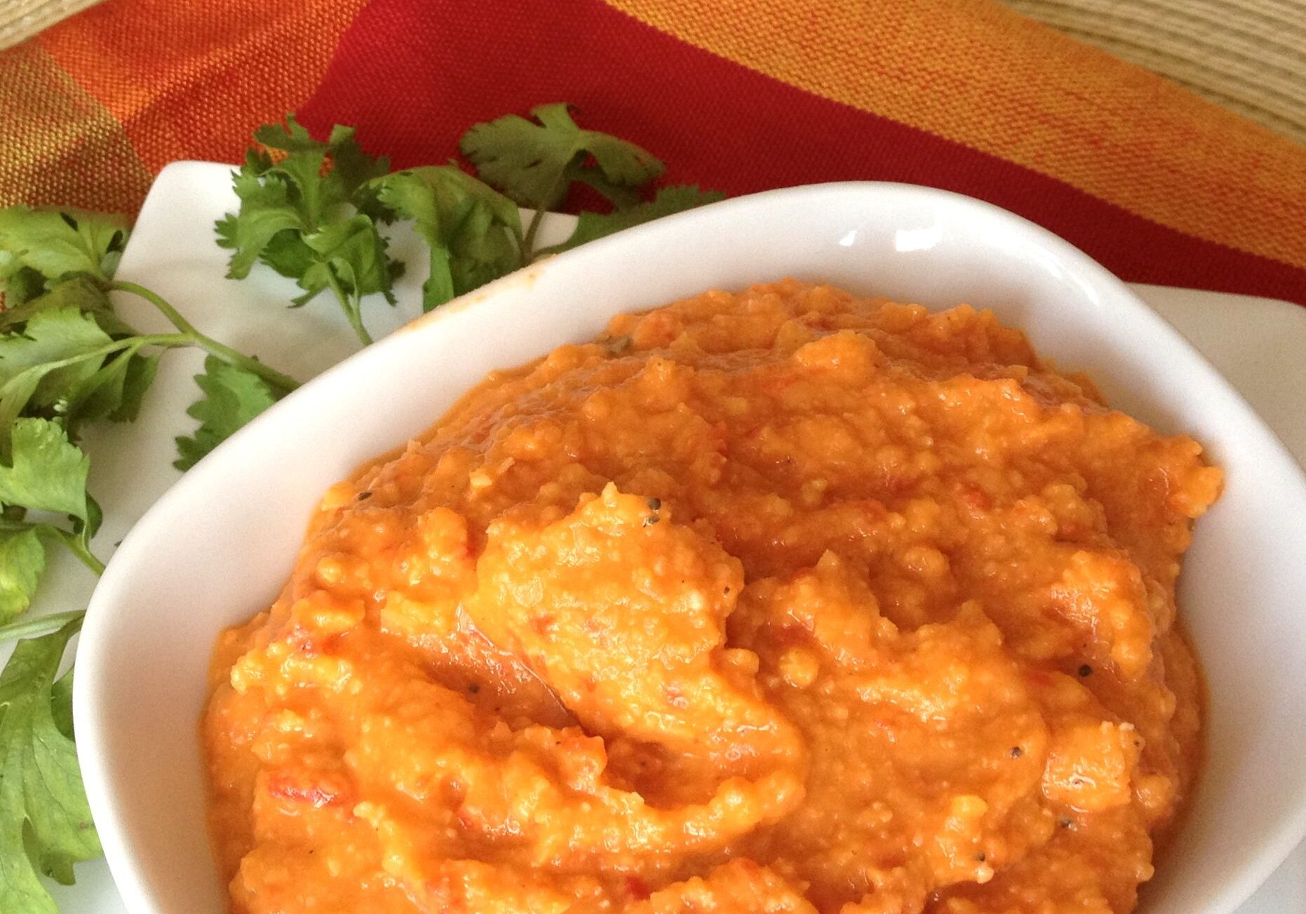 A bowl of creamy orange carrot puree with herbs on the side.