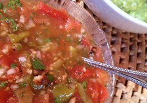 A bowl of fresh salsa with a spoon and a green dip in the background.