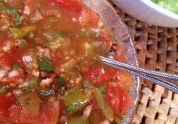 A bowl of fresh salsa with a spoon and guacamole in the background.