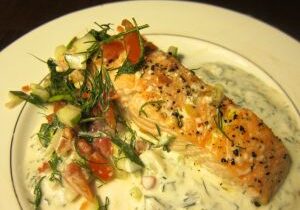 Grilled salmon topped with herbs and served with creamy sauce and vegetables.