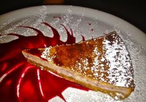 A slice of pie with powdered sugar and raspberry sauce.