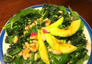 Fresh spinach salad with cashews, mango slices, and a lemon wedge.