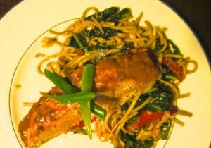 A plate of stir-fried noodles with vegetables and a crab claw.