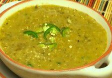 A bowl of thick green lentil soup garnished with green chili slices.