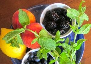 Fresh berries and peaches with mint on a wooden table.