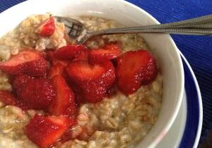 Bowl of oatmeal topped with sliced strawberries and a spoon.