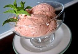 Two scoops of pink ice cream in a glass bowl with a mint garnish.