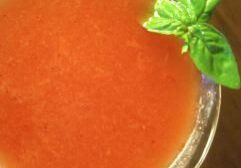 A glass of fresh tomato juice garnished with a basil leaf.