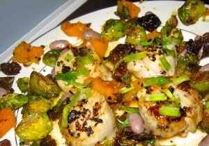 A colorful roasted vegetable and scallop dish with herbs and spices.
