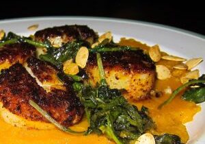 Seared scallops with greens and a creamy sauce on a white plate.