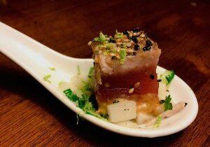 Gourmet tuna tartare served on a white porcelain spoon with herbs.