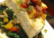 Grilled white fish topped with a colorful vegetable salsa on a bed of sautéed greens.