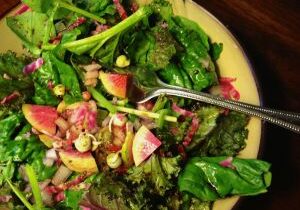 A fresh mixed green salad with spinach, radishes, and nuts.