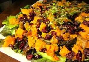 A vibrant salad with greens, orange cheese, and dried cranberries.