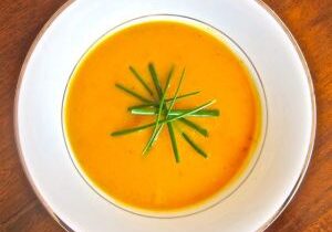 Creamy orange soup garnished with fresh green herbs in a white bowl.