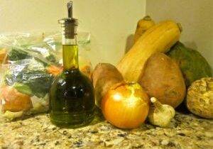 A bottle of olive oil with fresh vegetables on a kitchen counter.