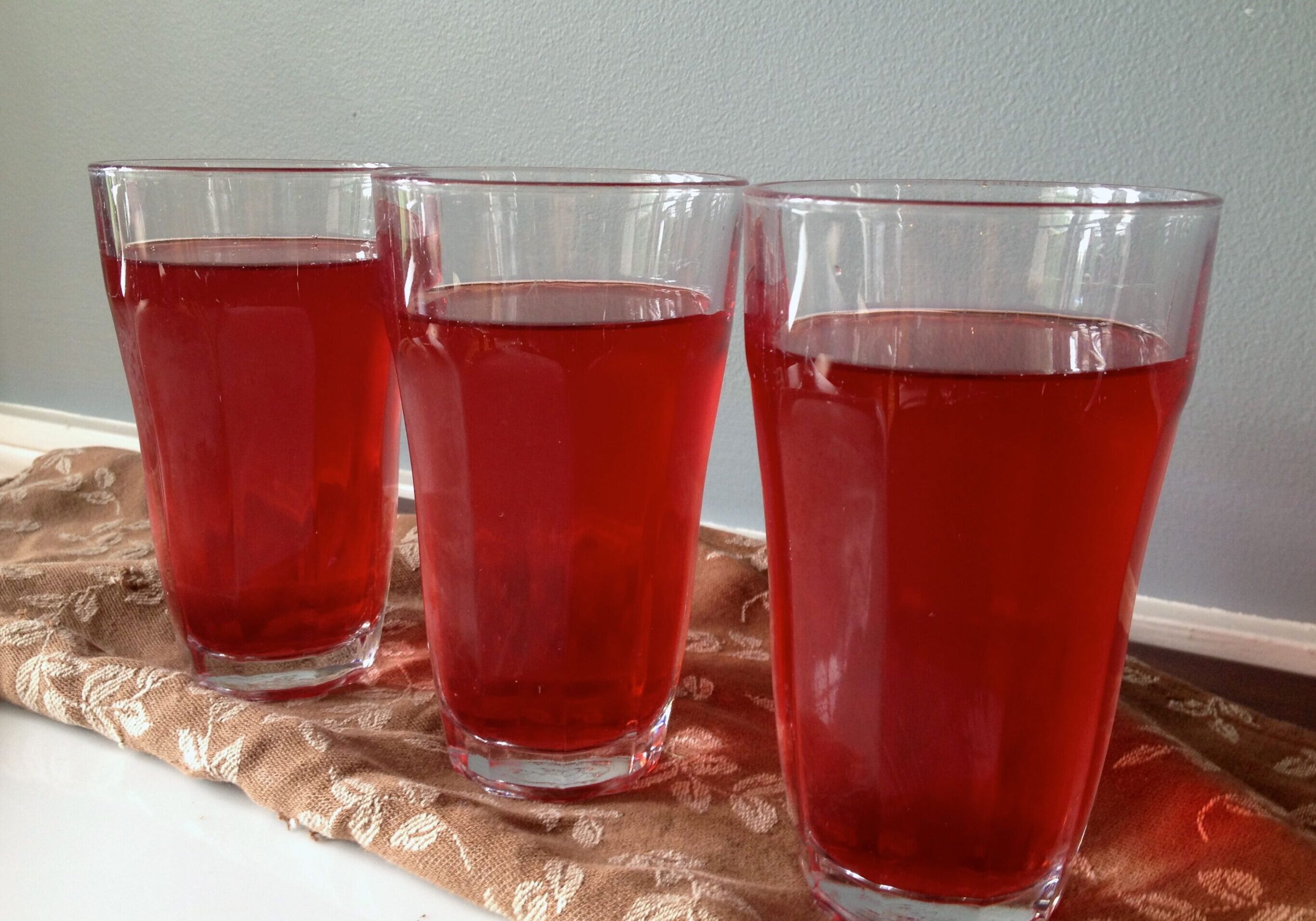 Three glasses filled with red liquid on a table.
