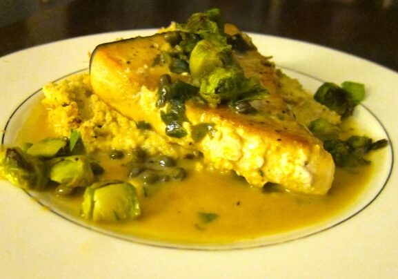 Seared fish steak with a creamy caper sauce garnish.
