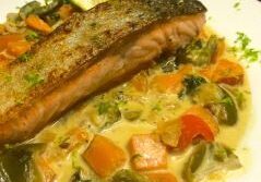 Grilled salmon served with creamy vegetable sauce and lime wedge.
