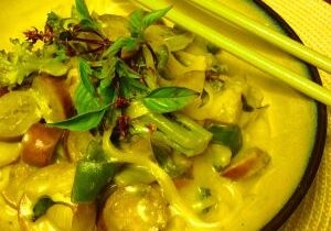 A bowl of creamy green curry with vegetables and mushrooms, served with chopsticks.