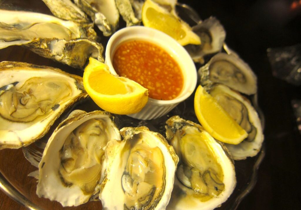 A platter of fresh oysters with lemon wedges and dipping sauce.