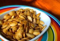Roasted pumpkin seeds served in a white bowl on a colorful plate.