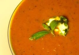 A bowl of creamy tomato soup garnished with herbs and cream.