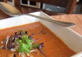 Creamy tomato soup garnished with herbs and microgreens.