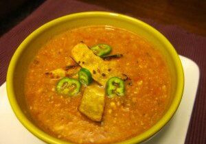 A bowl of spicy lentil curry garnished with green chili and fried potato pieces.