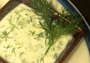 Creamy dill sauce garnished with fresh dill sprigs in a square dish.