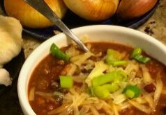 A bowl of chili topped with shredded cheese and green onions.