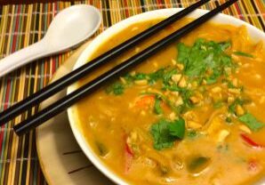 A bowl of creamy noodle soup garnished with herbs and chopsticks.