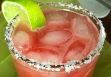 A refreshing pink cocktail with ice, lime wedges, and a salted rim.