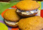 Three pumpkin whoopie pies with cream filling on a colorful plate.